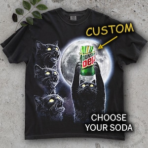 May include: Black t-shirt featuring a graphic of black cats with glowing yellow eyes, a full moon, and a Mountain Dew can. The text "CUSTOM" and "CHOOSE YOUR SODA" are also on the shirt.