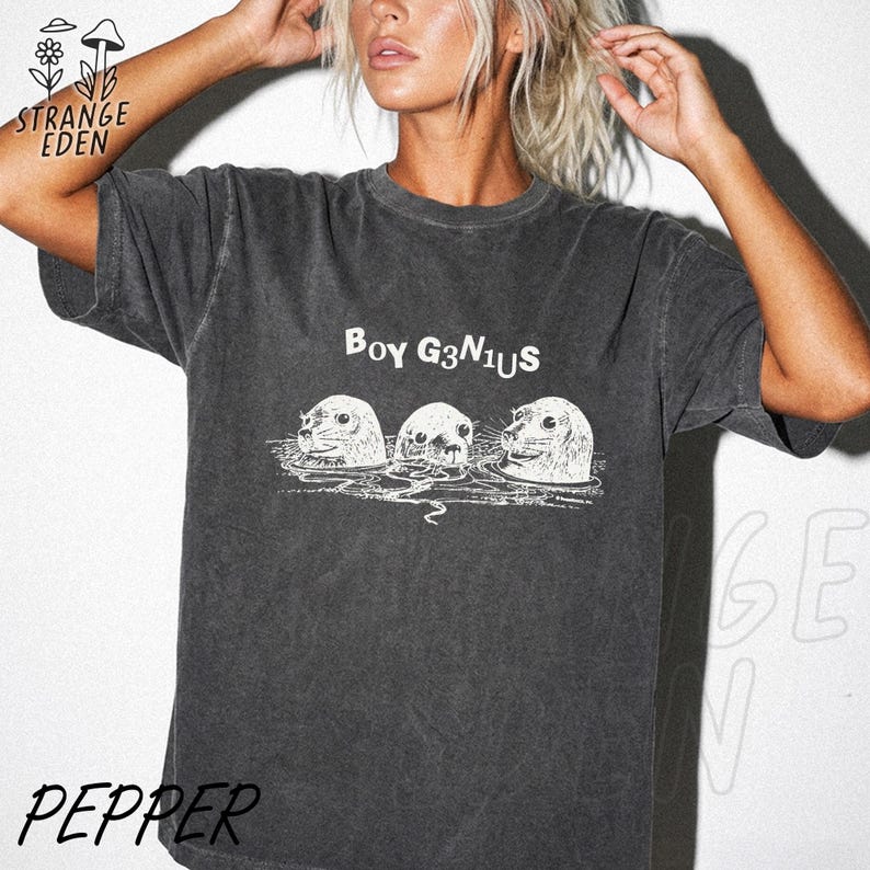 K&ouml;nnte beinhalten: Ein anthrazitfarbenes Kurzarm-T-Shirt mit einem wei&szlig;en Grafikdruck von drei Robben im Wasser. Der Text "BOY G3N1US" ist in Wei&szlig; &uuml;ber den Robben aufgedruckt. Der Stoff des Kleidungsst&uuml;cks weist eine verwaschene, vintageartige Textur auf.