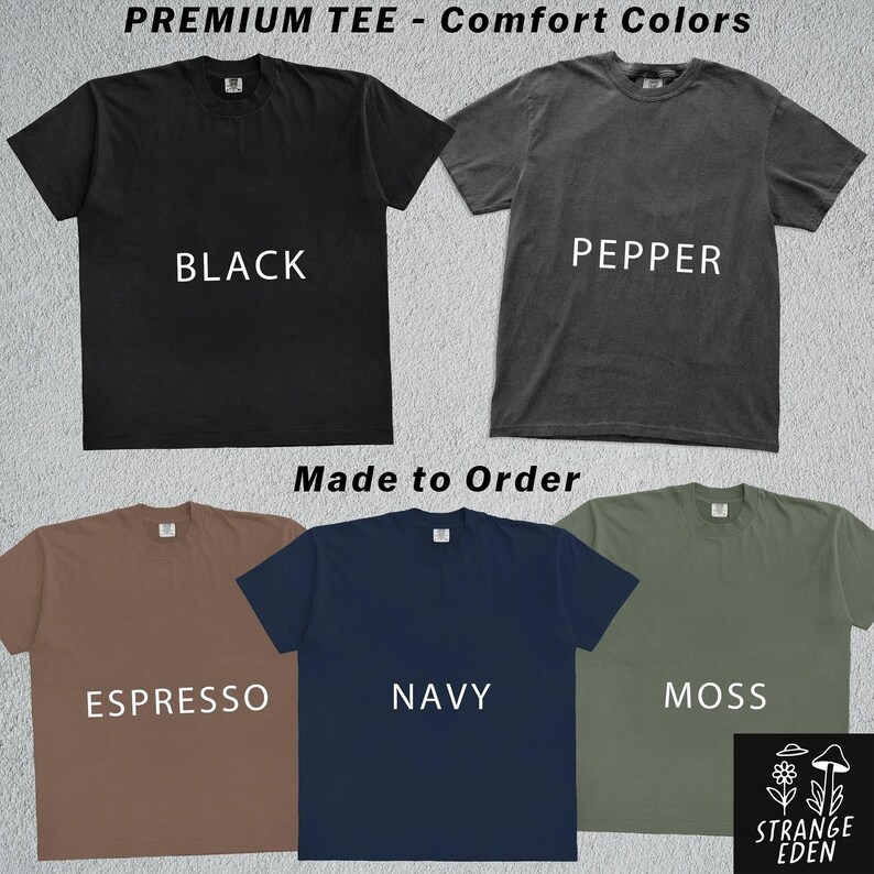 K&ouml;nnte beinhalten: F&uuml;nf kurz&auml;rmelige T-Shirts mit Rundhalsausschnitt in den Farben Schwarz, Pfeffer, Espresso, Marineblau und Moosgr&uuml;n. Der Text PREMIUM TEE - Comfort Colors, Made to Order und der Markenname STRANGE EDEN mit Pilz- und Blumengrafik sind zu sehen.