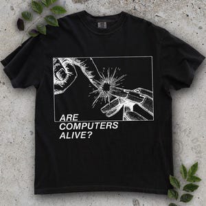 May include: Black t-shirt featuring a white graphic of hands interacting with a burst of light, with the text "ARE COMPUTERS ALIVE?" below. The shirt is made of a soft material and has a crew neck. A casual, everyday wear item.
