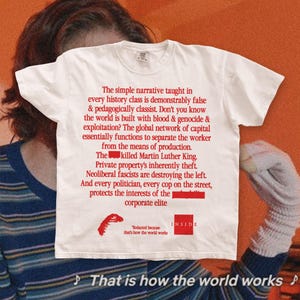 May include: A white short-sleeved t-shirt featuring red text that reads: The simple narrative taught in every history class is demonstrably false & pedagogically classist. Don't you know the world is built with blood & genocide & exploitation?