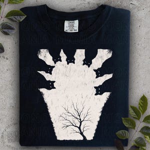 May include: Black t-shirt featuring a white graphic of black cats surrounding a tree. The design has a vintage, slightly distressed look. The shirt has a Comfort Colors tag, size XL-TG-EG.