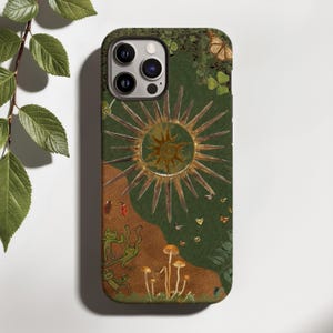May include: A phone case featuring a dark green and brown background with a central golden sun illustration. The design includes small drawings of frogs, mushrooms, butterflies, ladybugs, and clover leaves scattered across the surface.