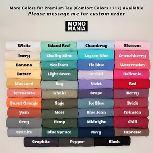 Op de afbeelding: Een display van opgevouwen t-shirts in verschillende kleuren, waaronder wit, blauw, groen en roze. Elk shirt is gelabeld met zijn kleurnaam, zoals "White", "Island Reef" en "Chambray". Het merklogo "MONO MANIA" is zichtbaar.