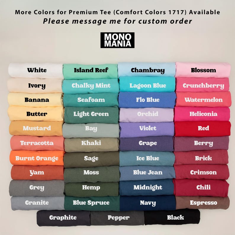 Op de afbeelding: Een display van opgevouwen t-shirts in verschillende kleuren, waaronder wit, blauw, groen en roze. Elk shirt is gelabeld met zijn kleurnaam, zoals "White", "Island Reef" en "Chambray". Het merklogo "MONO MANIA" is zichtbaar.