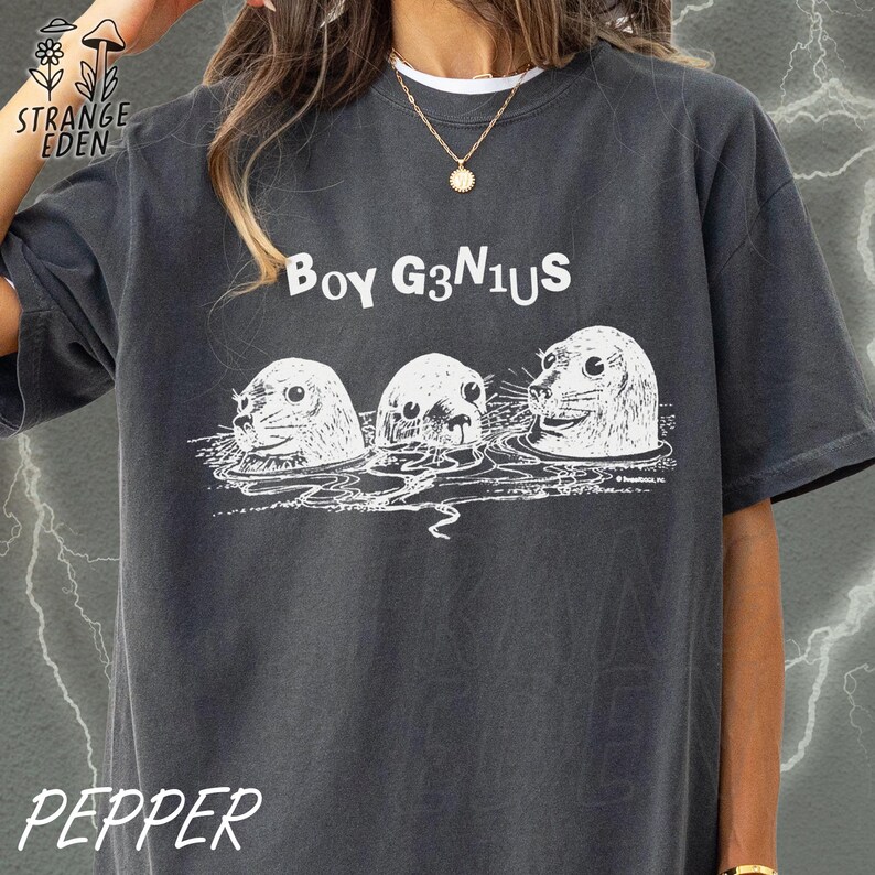 K&ouml;nnte beinhalten: Ein anthrazitfarbenes Kurzarm-T-Shirt mit einem wei&szlig;en Grafikdruck von drei aus dem Wasser ragenden Robbenk&ouml;pfen. Der Text "BOY G3N1US" ist in Wei&szlig; &uuml;ber den Robben aufgedruckt. Das T-Shirt hat einen Rundhalsausschnitt und eine lockere Passform.