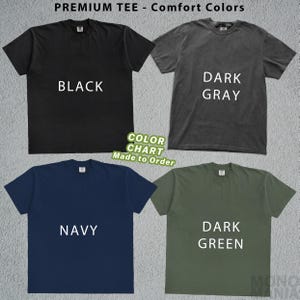 Peut inclure: Un nuancier de quatre t-shirts noirs, gris fonc&eacute;, marine et vert fonc&eacute;. Chaque chemise affiche son nom de couleur en texte blanc. Le haut de l'image indique "PREMIUM TEE - Comfort Colors". Un autocollant vert dit "COLOR CHART Made to Order".