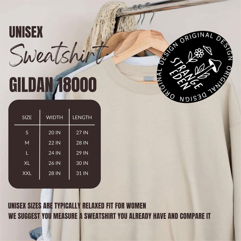 Puede incluir: Una sudadera unisex Gildan 18000 de color beige colgada en una percha de madera. Una tabla marr&oacute;n oscuro muestra las tallas de S a XXL con medidas de ancho y largo en pulgadas. Un logotipo negro circular presenta una flor, un hongo y el texto Strange Eden.