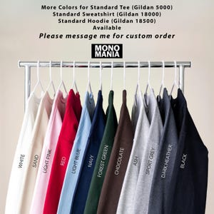 May include: A rack of Gildan brand sweatshirts and hoodies in various colors, including white, sand, light pink, red, light blue, navy, forest green, chocolate, ash, sport grey, dark heather, and black. The brand name "MONO MANIA" is displayed.