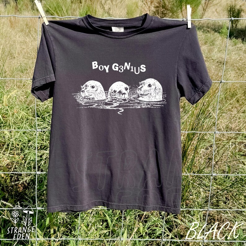K&ouml;nnte beinhalten: Ein anthrazitfarbenes Kurzarm-T-Shirt mit einem wei&szlig;en Grafikdruck von drei Robben im Wasser. &Uuml;ber den Robben steht der Text BOY G3N1US in einer fetten, stilisierten Schriftart. Das T-Shirt hat einen Rundhalsausschnitt und eine Standardpassform.