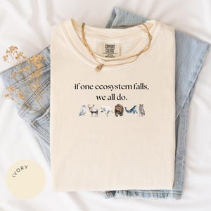 May include: Ivory t-shirt with the text "if one ecosystem falls, we all do." and a line of illustrated animals including a bird, deer, polar bear, bear, whale, and wolf.