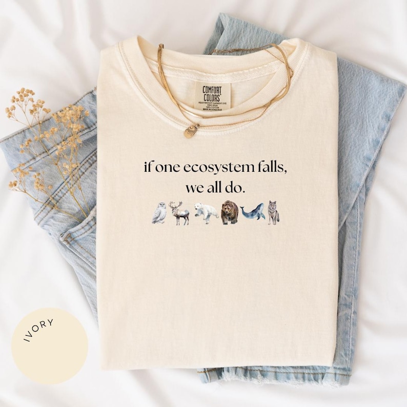 May include: Ivory t-shirt with the text "if one ecosystem falls, we all do." and a line of illustrated animals including a bird, deer, polar bear, bear, whale, and wolf.