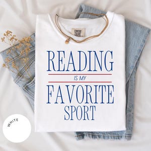 以下が含まれることがあります： 白いTシャツに青い文字で「読書は私の好きなスポーツです」と書かれています。