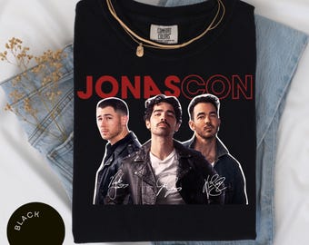 May include: Black t-shirt with a red graphic of the Jonas Brothers. The graphic includes their names "JONASCON" and their signatures.