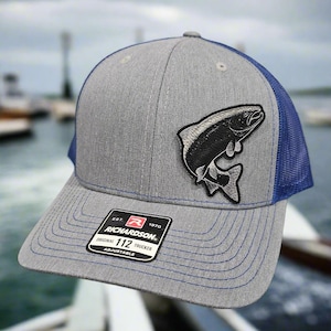 May include: Gray and blue trucker hat with a black and white fish patch. The hat has a Richardson 112 Original Trucker label.