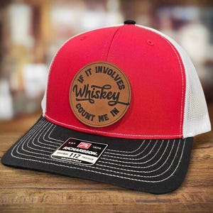 May include: Red and black trucker hat with a brown leather patch that says "If it involves whiskey count me in".