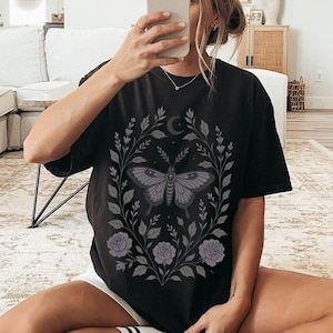 May include: Black oversized t-shirt with a floral design featuring a butterfly and a crescent moon.