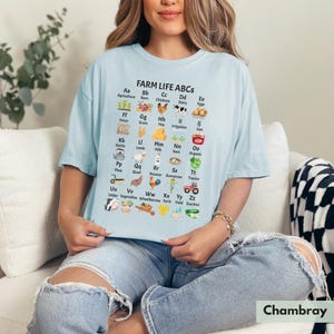 May include: A light blue t-shirt featuring a graphic of farm-related items and the text "FARM LIFE ABCS" with each letter of the alphabet paired with a farm-related word. For example, "Aa Agriculture", "Bb Barn", "Cc Chickens", "Dd Dairy", "Ee Eggs", "Ff Fence", "Gg Grain", "Hh Hay", "Ii Irrigation", "Jj Jam", "Kk Kettle", "Ll Lamb", "Mm Milk", "Nn Nest", "Oo Organic", "Pp Plow", "Qq Quail", "Rr Rooster", "Ss Scarecrow", "Tt Tractor", "Uu Udder", "Vv Vegetables", "Ww Wheelbarrow", "Xx Xyris", "Yy Yield", "Zz Zucchini".
