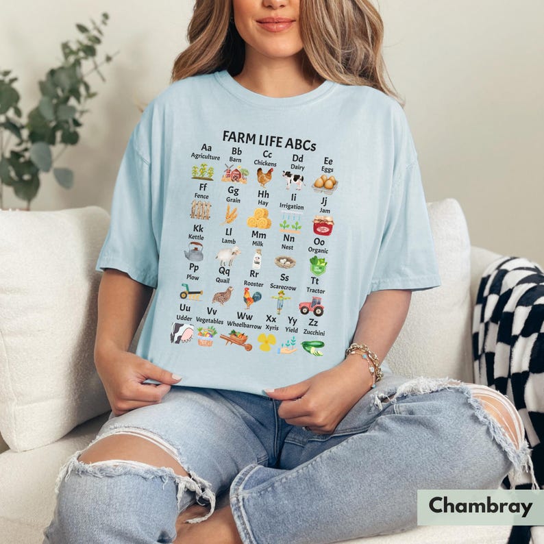 May include: A light blue t-shirt featuring a graphic of farm-related items and the text "FARM LIFE ABCS" with each letter of the alphabet paired with a farm-related word. For example, "Aa Agriculture", "Bb Barn", "Cc Chickens", "Dd Dairy", "Ee Eggs", "Ff Fence", "Gg Grain", "Hh Hay", "Ii Irrigation", "Jj Jam", "Kk Kettle", "Ll Lamb", "Mm Milk", "Nn Nest", "Oo Organic", "Pp Plow", "Qq Quail", "Rr Rooster", "Ss Scarecrow", "Tt Tractor", "Uu Udder", "Vv Vegetables", "Ww Wheelbarrow", "Xx Xyris", "Yy Yield", "Zz Zucchini".