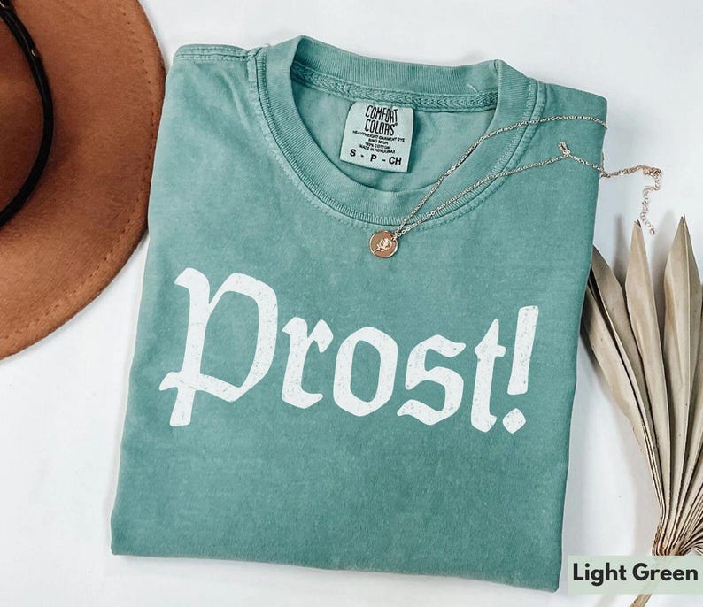 Puede incluir: Camiseta verde claro con la palabra "Prost!" impresa en blanco en la parte delantera. La camiseta est&aacute; hecha de un material suave y c&oacute;modo y tiene un corte holgado.