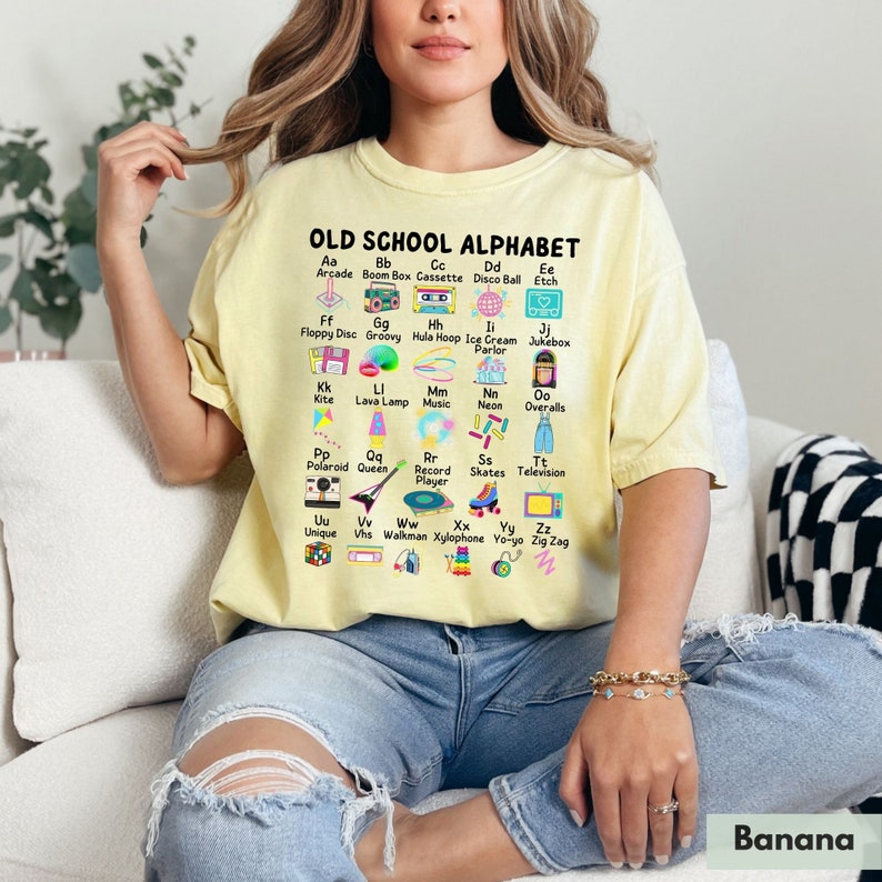May include: A yellow t-shirt with a graphic print of an alphabet with retro icons. The text reads "OLD SCHOOL ALPHABET".