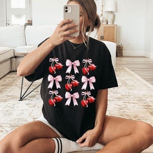 May include: Black t-shirt with a graphic print of red cherries with pink bows.