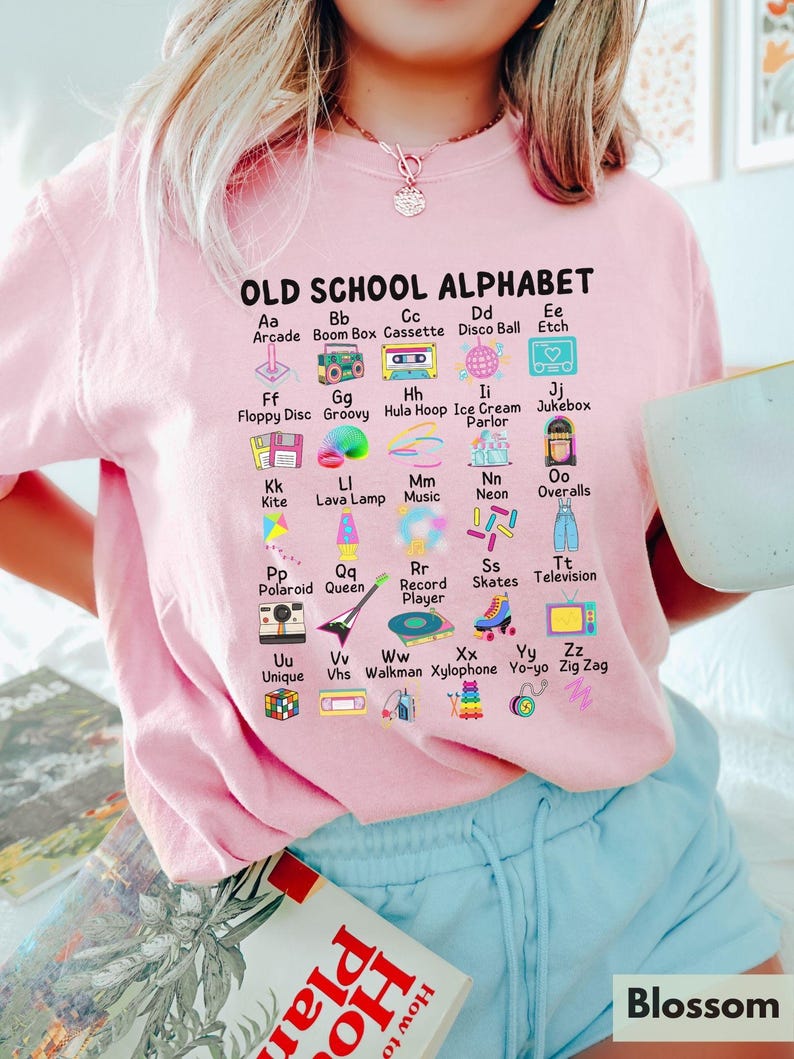 May include: Pink t-shirt with a graphic of an alphabet with old school items like a boom box, cassette tape, and a hula hoop. The text reads "OLD SCHOOL ALPHABET".