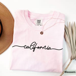 May include: A pink t-shirt with the word "california" written in black cursive script.