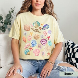 Op de afbeelding: Een geel T-shirt met een kleurrijk schelpmotief. Het shirt heeft een losse pasvorm en een ronde hals.