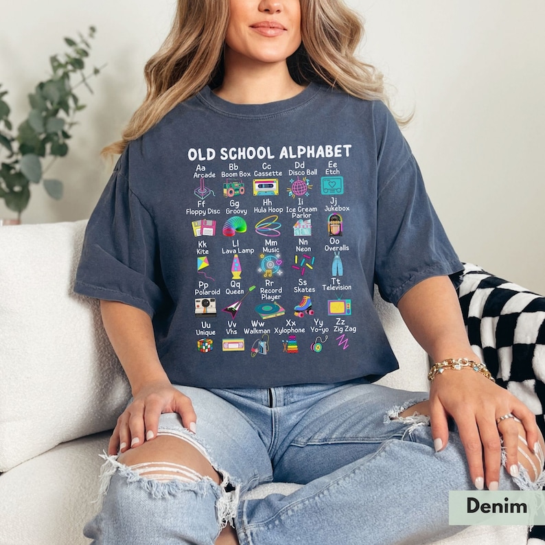May include: A blue t-shirt with a graphic of an old school alphabet. Each letter is represented by a retro icon, such as a boom box, a cassette tape, a hula hoop, a record player, and a walkman. The text "OLD SCHOOL ALPHABET" is printed at the top of the graphic.