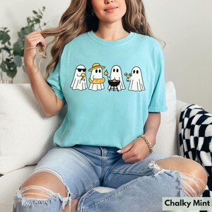 May include: A light blue t-shirt with a graphic of four cartoon ghosts enjoying summer activities. One ghost wears sunglasses, another a hat and floatie, one grills, and the last holds a cocktail. The text "Chalky Mint" is at the bottom.