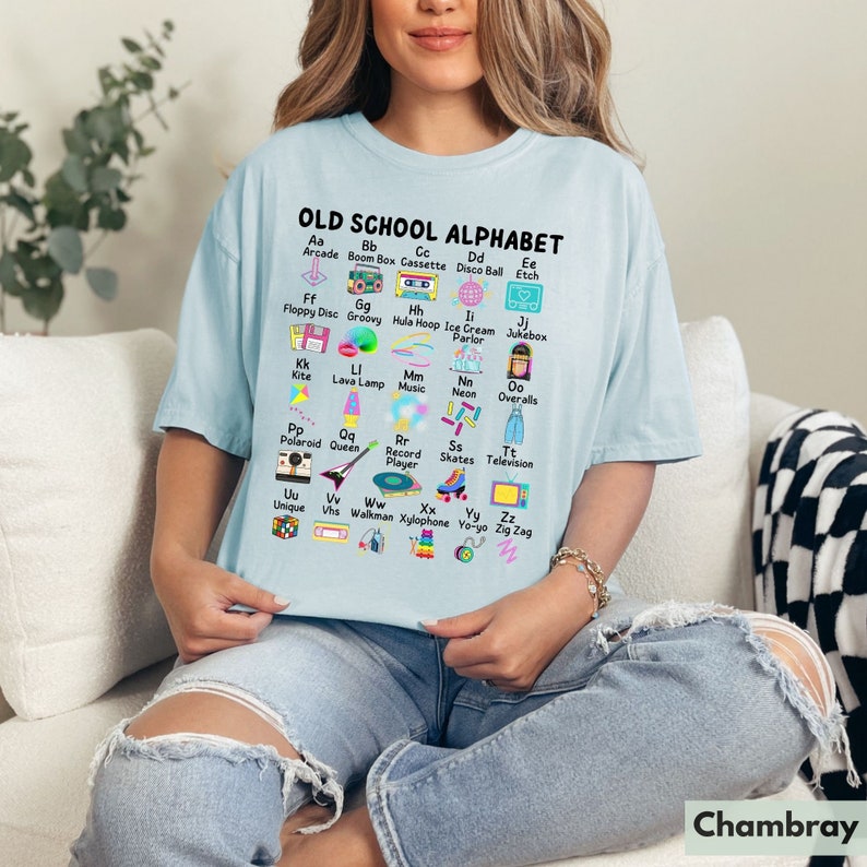 May include: A light blue t-shirt with a graphic of an alphabet printed on it. The graphic features a different 80s themed icon for each letter of the alphabet. The text "OLD SCHOOL ALPHABET" is printed at the top of the graphic.