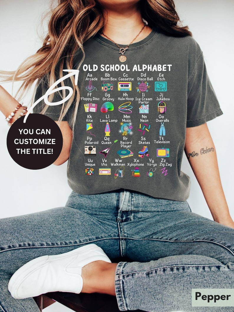 May include: A gray t-shirt with a graphic of an alphabet with retro icons. The text reads "OLD SCHOOL ALPHABET" and includes icons for each letter. The text "YOU CAN CUSTOMIZE THE TITLE!" is also on the shirt.
