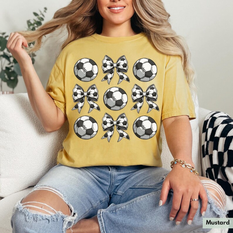 Puede incluir: Una camiseta amarilla mostaza con un patr&oacute;n de balones de f&uacute;tbol blanco y negro y lazos.