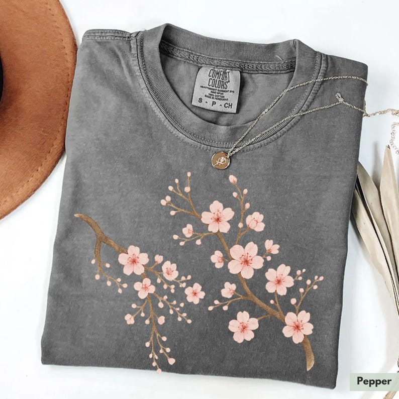 May include: A gray t-shirt with a pink cherry blossom design. The shirt has a tag that says "Comfort Colors" and "S - P - CH".