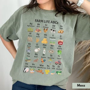 May include: A green t-shirt with a white print of the alphabet with farm-related illustrations and the text "FARM LIFE ABCS".