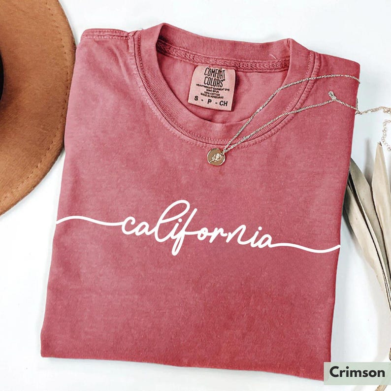 May include: A crimson red t-shirt with the word "california" written in white cursive script. The shirt has a tag that reads "Comfort Colors" and "S - P - CH".