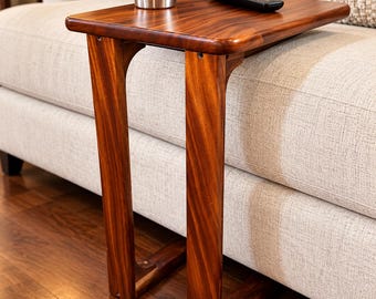 May include: A C-shaped side table crafted from polished dark brown wood with a smooth rectangular top and two vertical legs that extend to a base, supporting a stainless steel tumbler and a black television remote control.