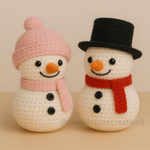 Two crocheted amigurumi snowmen with different accessories: one with a pink beanie and scarf, and one with a black top hat and red scarf, displayed on a wooden surface.