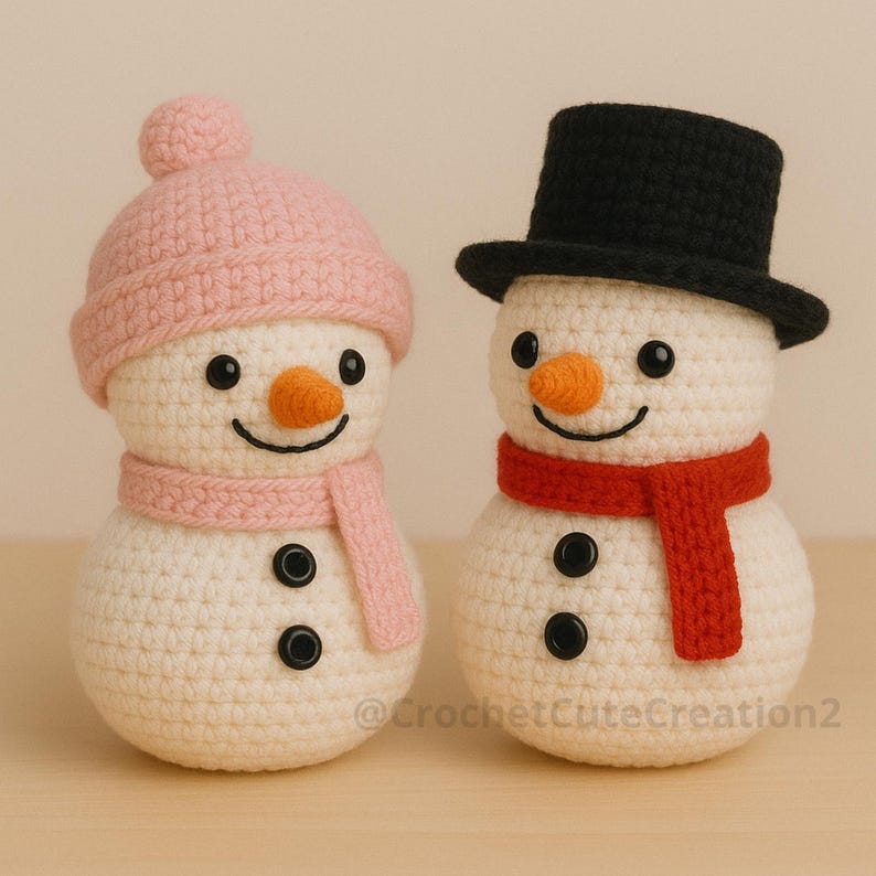 Two crocheted amigurumi snowmen with different accessories: one with a pink beanie and scarf, and one with a black top hat and red scarf, displayed on a wooden surface.