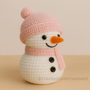 Puede incluir: Un mu&ntilde;eco de nieve de ganchillo hecho a mano, con gorro y bufanda rosas, una peque&ntilde;a nariz naranja y ojos de bot&oacute;n negros. El mu&ntilde;eco de nieve es blanco, con una sonrisa cosida. La figura mide unos 13 cm de alto.