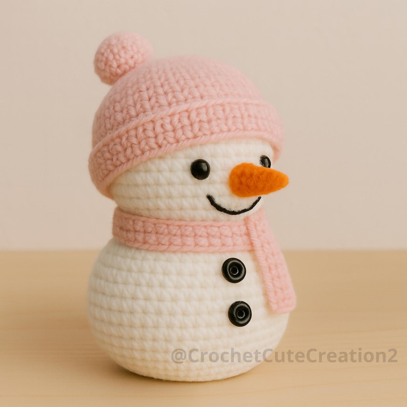 Puede incluir: Un mu&ntilde;eco de nieve de ganchillo hecho a mano, con gorro y bufanda rosas, una peque&ntilde;a nariz naranja y ojos de bot&oacute;n negros. El mu&ntilde;eco de nieve es blanco, con una sonrisa cosida. La figura mide unos 13 cm de alto.