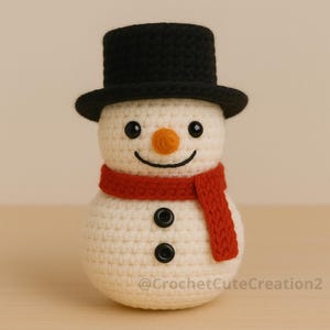Puede incluir: Un mu&ntilde;eco de nieve tejido a ganchillo con un sombrero de copa negro, una bufanda roja y ojos y botones negros. El mu&ntilde;eco de nieve tiene una nariz naranja y una boca sonriente. El texto "@CrochetCuteCreation2" es visible.