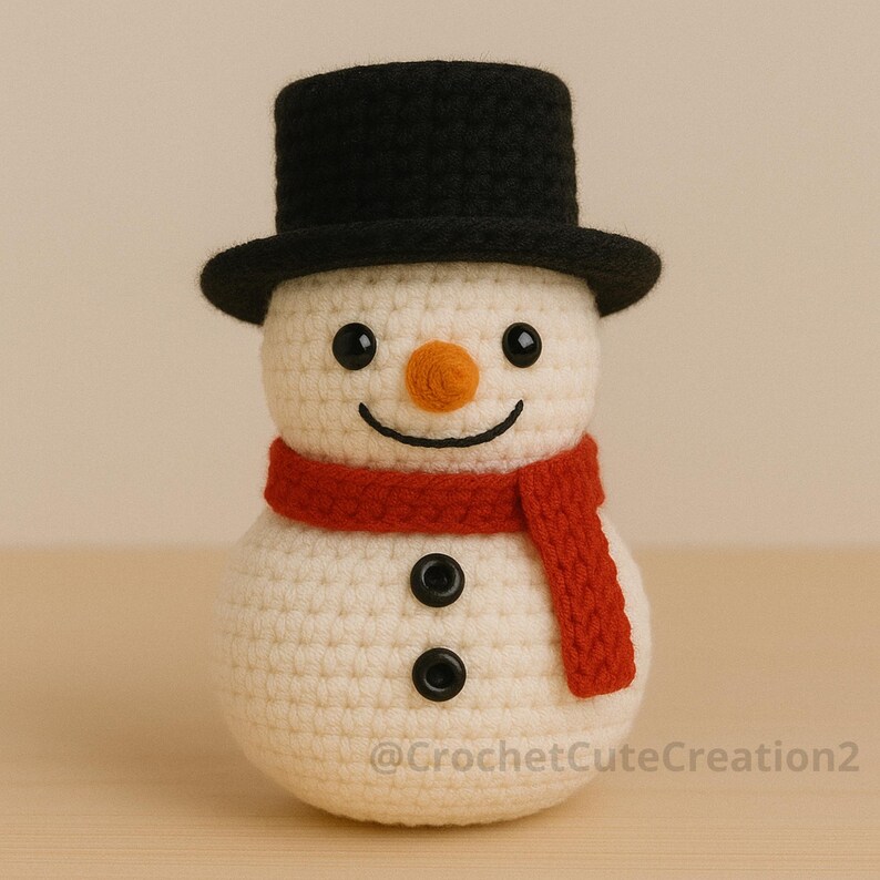 Puede incluir: Un mu&ntilde;eco de nieve tejido a ganchillo con un sombrero de copa negro, una bufanda roja y ojos y botones negros. El mu&ntilde;eco de nieve tiene una nariz naranja y una boca sonriente. El texto "@CrochetCuteCreation2" es visible.