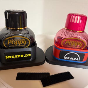 Könnte beinhalten: Zwei Grace Mate Poppy Flüssiglufterfrischer. Einer hat eine schwarze Flasche und einen schwarzen Deckel, der andere eine rosa Flasche und einen roten Deckel. Beide stehen in schwarzen Sockeln. Der Sockel der rosa Flasche hat ein rot-blau-weißes Design mit dem "MAN"-Logo.