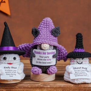 May include: Three crocheted figures: a white ghost wearing a black witch hat, a dark gray bat with a purple hat and wings, and a white ghost wearing a black and purple hat. Each figure holds a white card with printed text messages.