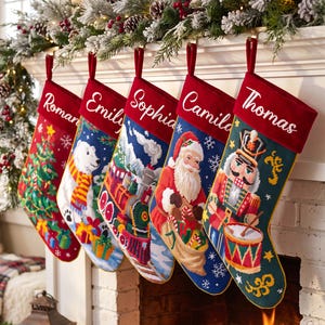 Könnte beinhalten: Fünf personalisierte Weihnachtsstrümpfe mit roten Samtbündchen und den Namen Roman, Emily, Sophia, Camila und Thomas. Jeder Strumpf zeigt ein einzigartiges Stickmotiv, darunter ein Weihnachtsbaum, ein Eisbär, ein Zug, der Weihnachtsmann und ein Nussknacker.