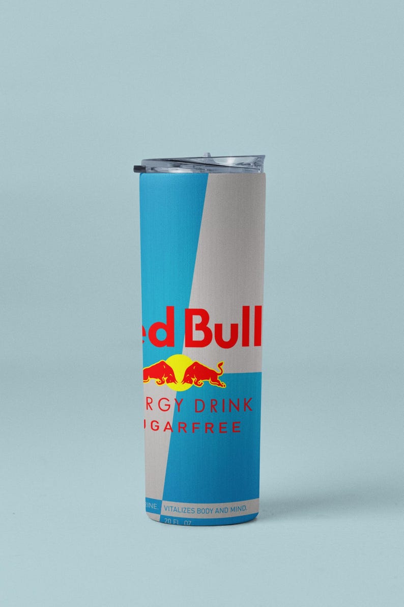 May include: A cylindrical, insulated tumbler with a clear lid. The tumbler features a blue and gray color scheme with the Red Bull logo and text. The text reads "ENERGY DRINK SUGARFREE" and "VITALIZES BODY AND MIND".