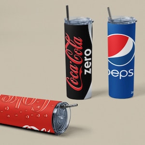 May include: Tumblers featuring Coca-Cola Zero, Pepsi, and a Coca-Cola design. The Coca-Cola Zero tumbler is black with red text. The Pepsi tumbler is blue with a red and white logo. The red Coca-Cola tumbler is lying down.