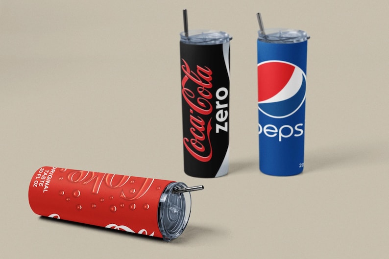 May include: Tumblers featuring Coca-Cola Zero, Pepsi, and a Coca-Cola design. The Coca-Cola Zero tumbler is black with red text. The Pepsi tumbler is blue with a red and white logo. The red Coca-Cola tumbler is lying down.